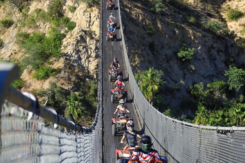 ATV riders crossing a suspension bridge over a desert canyon