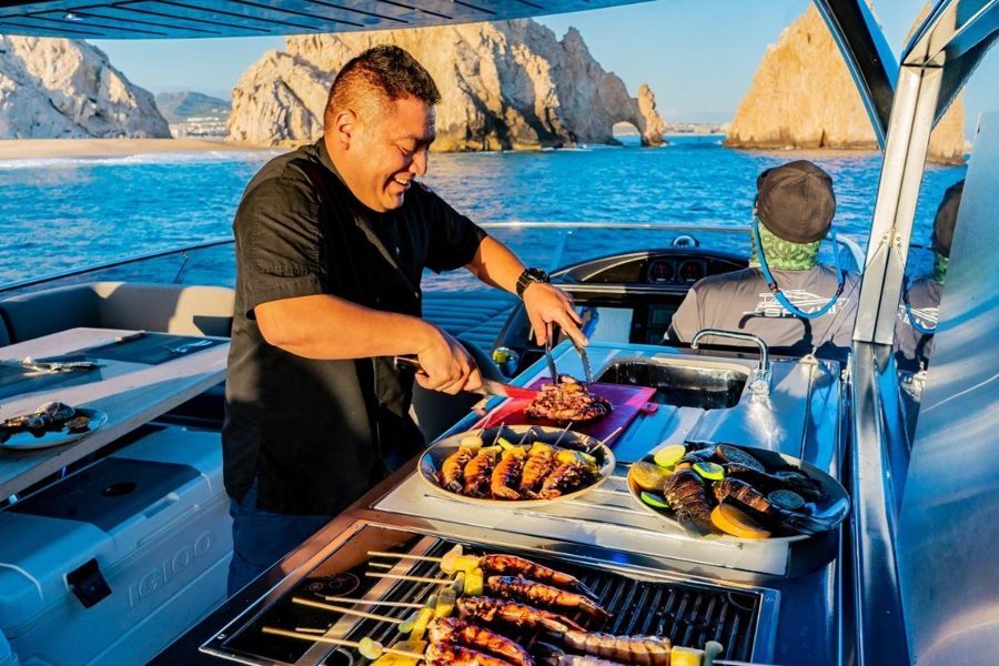 Private chef grilling on board a yacht with the Cabo Arch behind