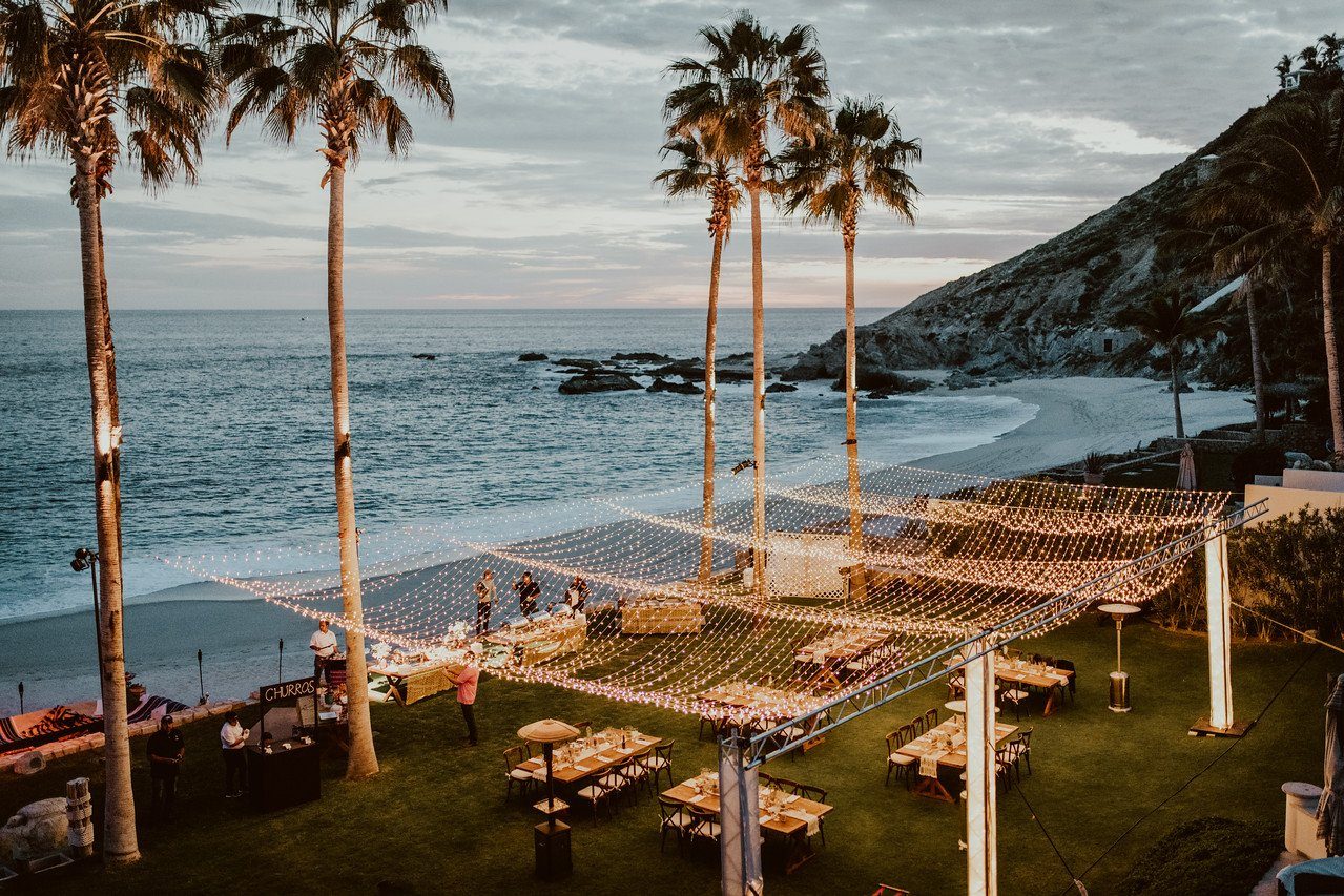 Reception tables under string lights on a seaside lawn at dusk